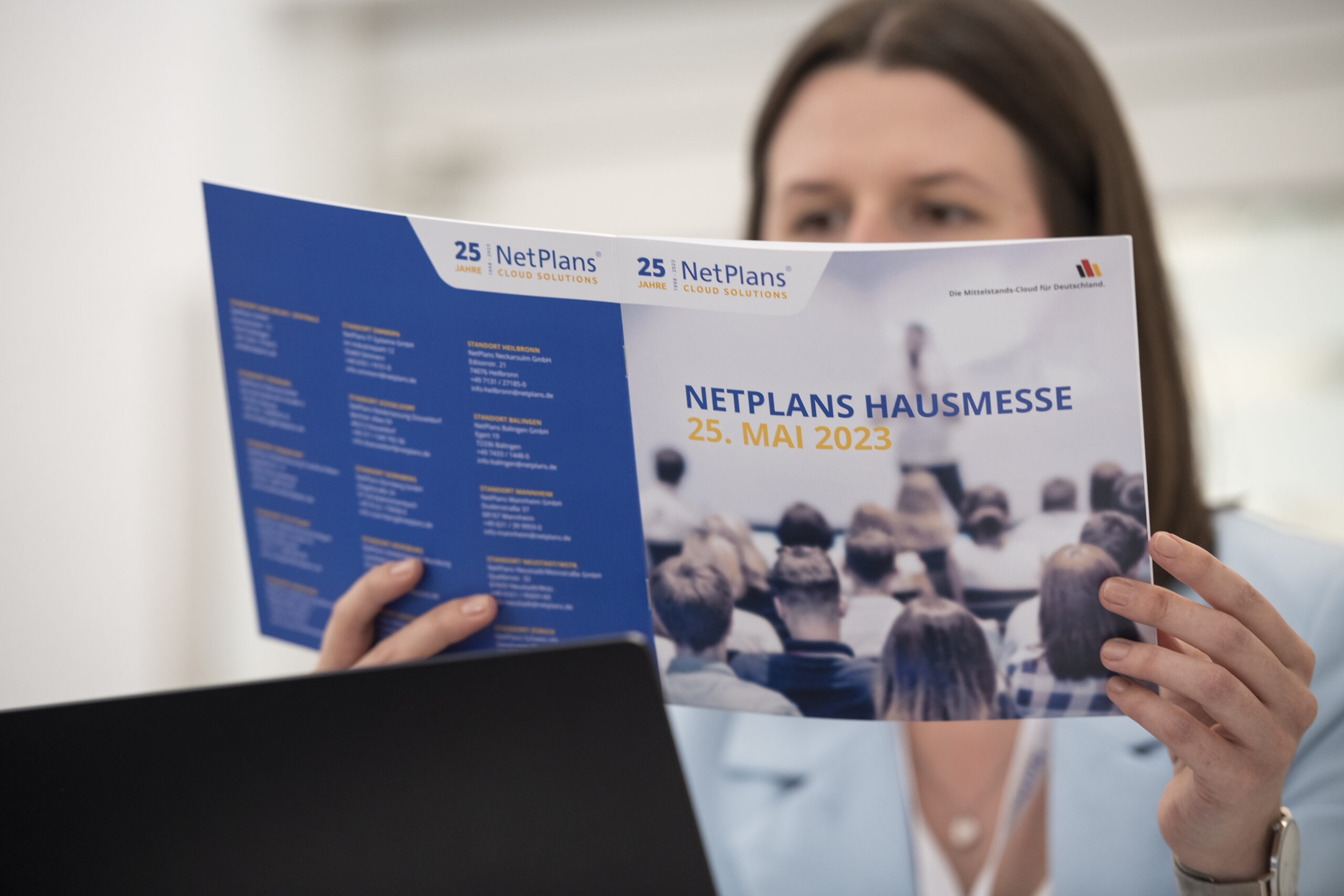 Frau in hellblauen Blazer hält die Teilnehmerbroschüre den NetPlans Hausmesse 2023 in ihren Händen