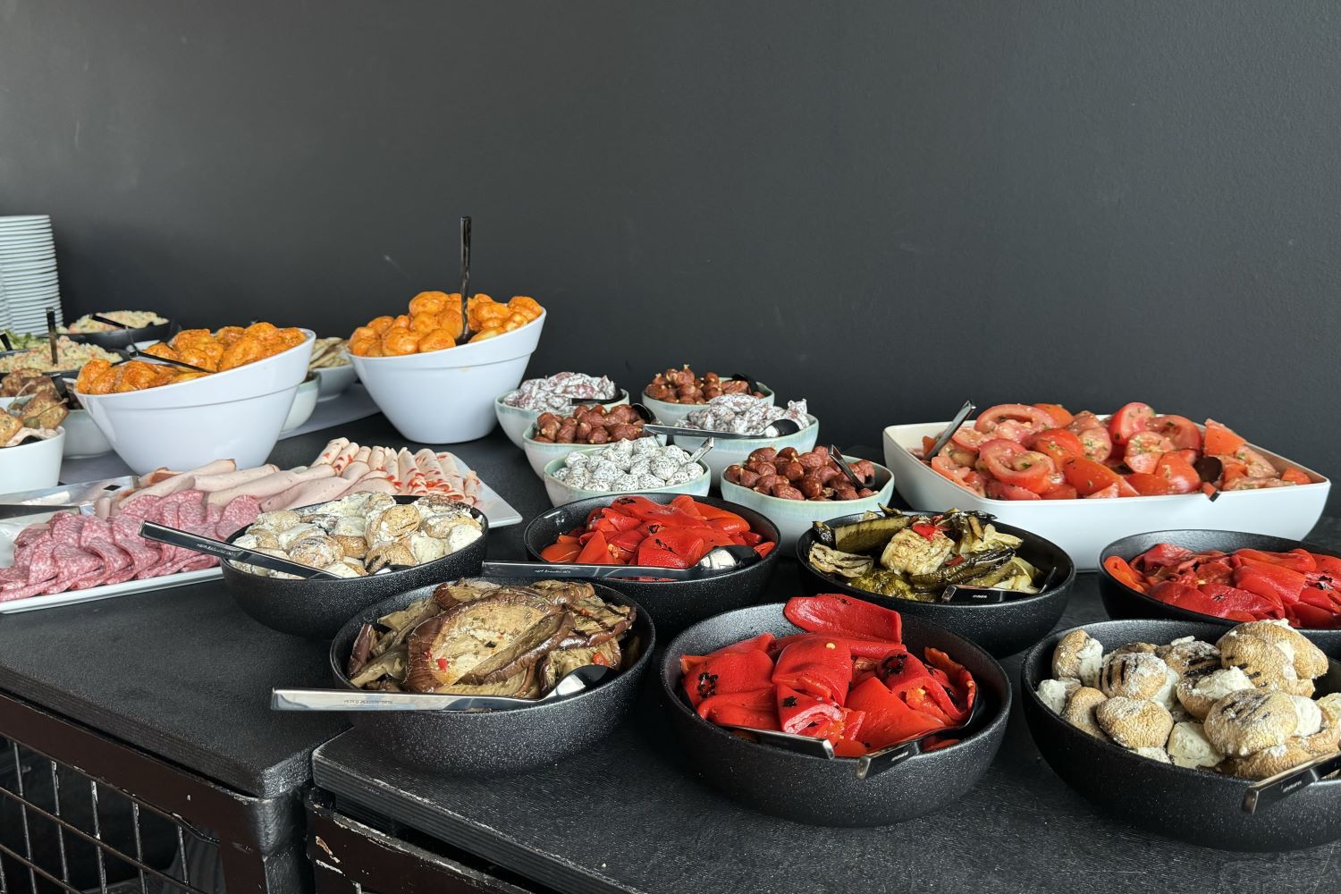 Buffet mit Antipasti, Kartoffeln und Wurstwaren alles in schwarzen und weißen Schüssel platziert.