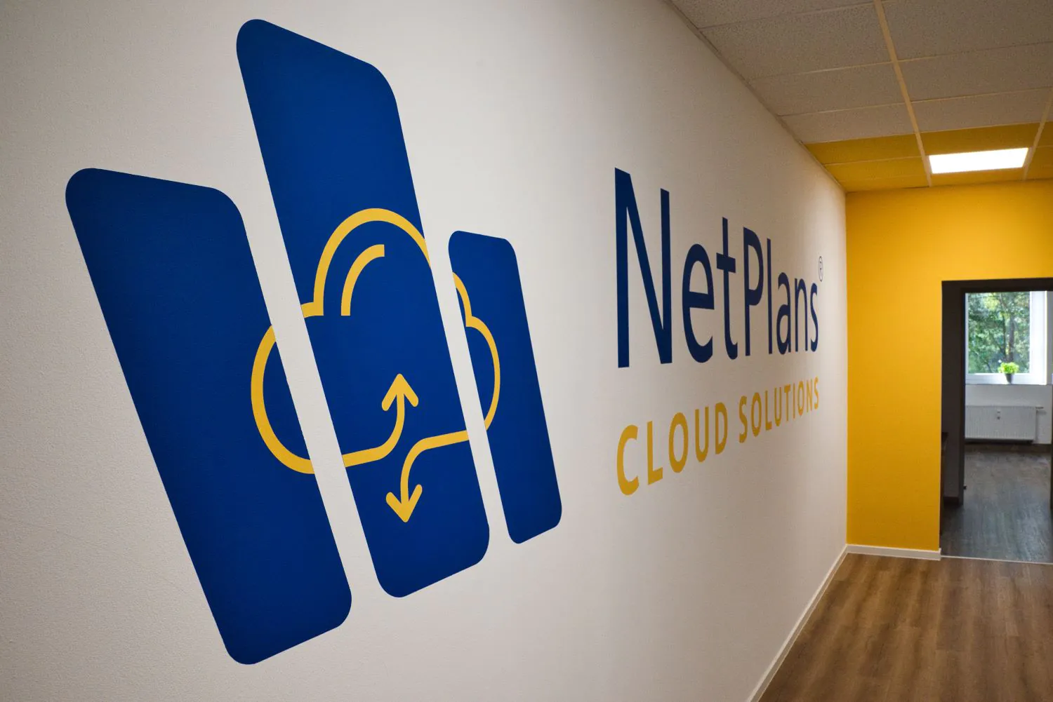 leerer Bürogang mit großem blau gelbem NetPlans Wandtattoo mit Motiv eines Icons einer Wolke