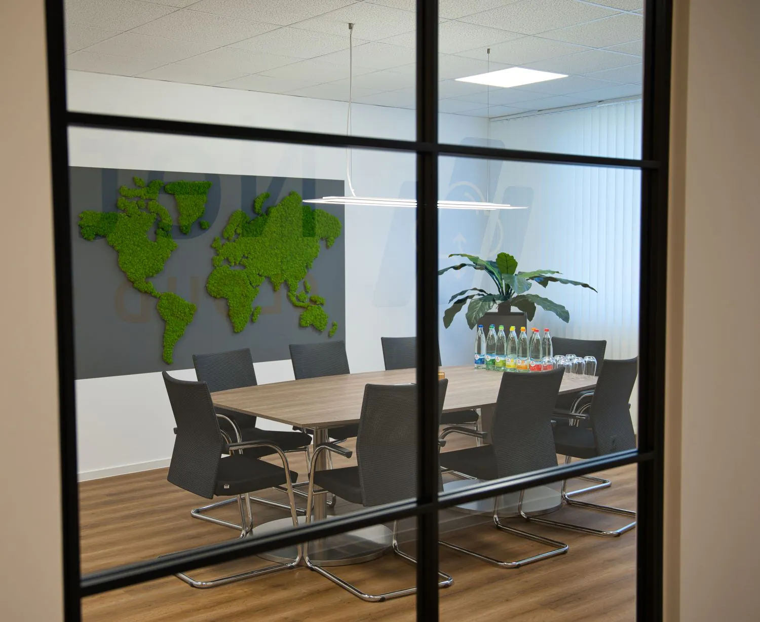 Blick vom Gang durch Glaswand in Konferenzraum mit Weltkarte als Graswand